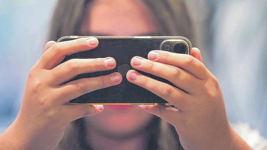 Una adolescente ante su teléfono móvil.