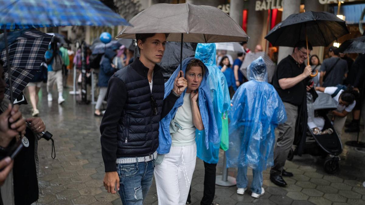Personas con chubasqueros y paraguas para salvaguardarse de la lluvia, en Barcelona.