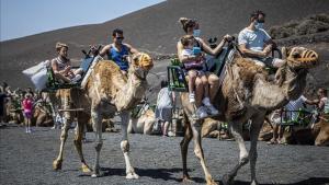 Turistas, protegidos con mascarillas, en camello por el Parque Nacional de Timanfaya, en Lanzarote.