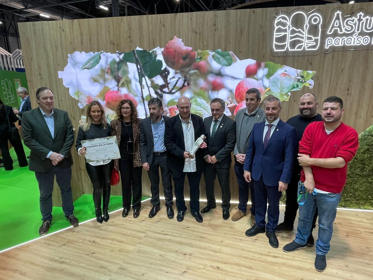 Álvarez-Aja, en el centro, con la escultura, y su hija Begoña, con el diploma, rodeados de los alcaldes de la Comarca de la Sidra, en Fitur.