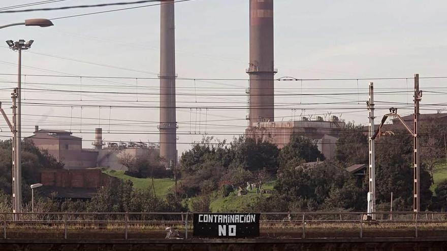 Pancarta colocada en el puente ferroviario de Veriña, con las chimeneas de Arcelor-Mittal al fondo.