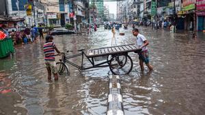 Dos hombres intentan mover su bicicleta de tres ruedas a través de la inundada Green Road en Dhaka tras las fuertes lluvias.