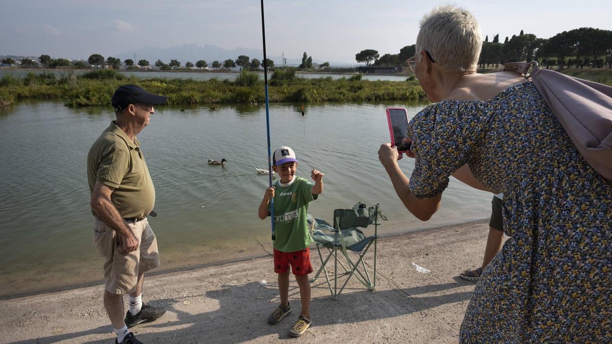 Un petit pescador mostra el peixet que ha pescat a la seva mare, que li fa una fotografia