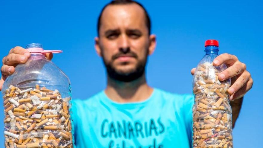 Luis Valien, fundador de Canarias Libre de Plásticos, sostiene dos botellas llenas de colillas recogidas en una playa de Gran Canaria