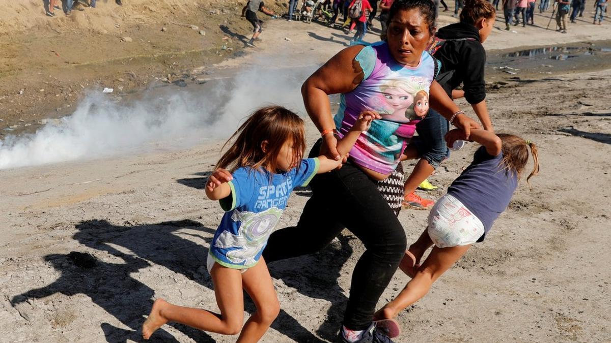 Una mujer hondureña huye con sus hijas de los gases lacrimógenos, este domingo en Tijuana.