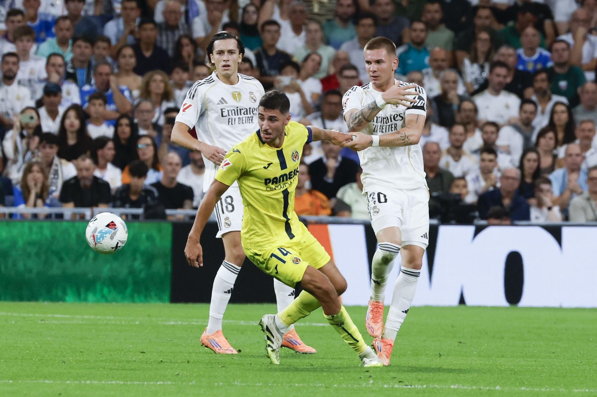 MADRID, 04/10/2025.- El centrocampista del Villareal Santi Comesaña (c) juega un balón entre Franco Mastantuono (d) y Álvaro Carreras, ambos del Real Madrid, durante el partido de LaLiga de fútbol que Real Madrid y Villarreal disputan este sábado en el estadio Santiago Bernabéu. EFE/Guillén