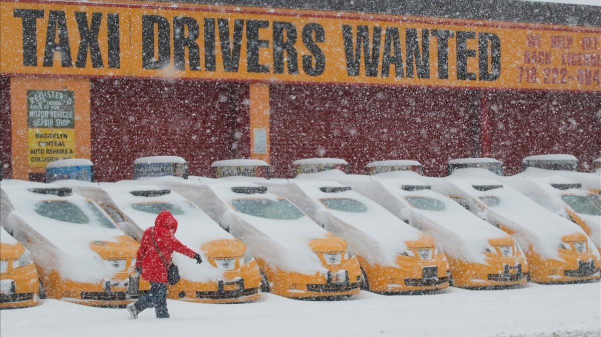Un peatón pasa delante delante de los taxis cubiertos de nieve en Nueva York 