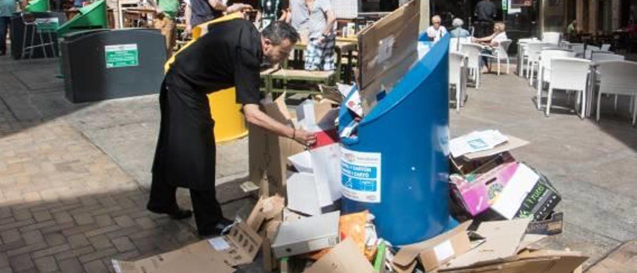 Un camarero deja cajas de cartón junto a uno de los contenedores soterrados de reciclaje atestado de residuos, ayer al mediodía.