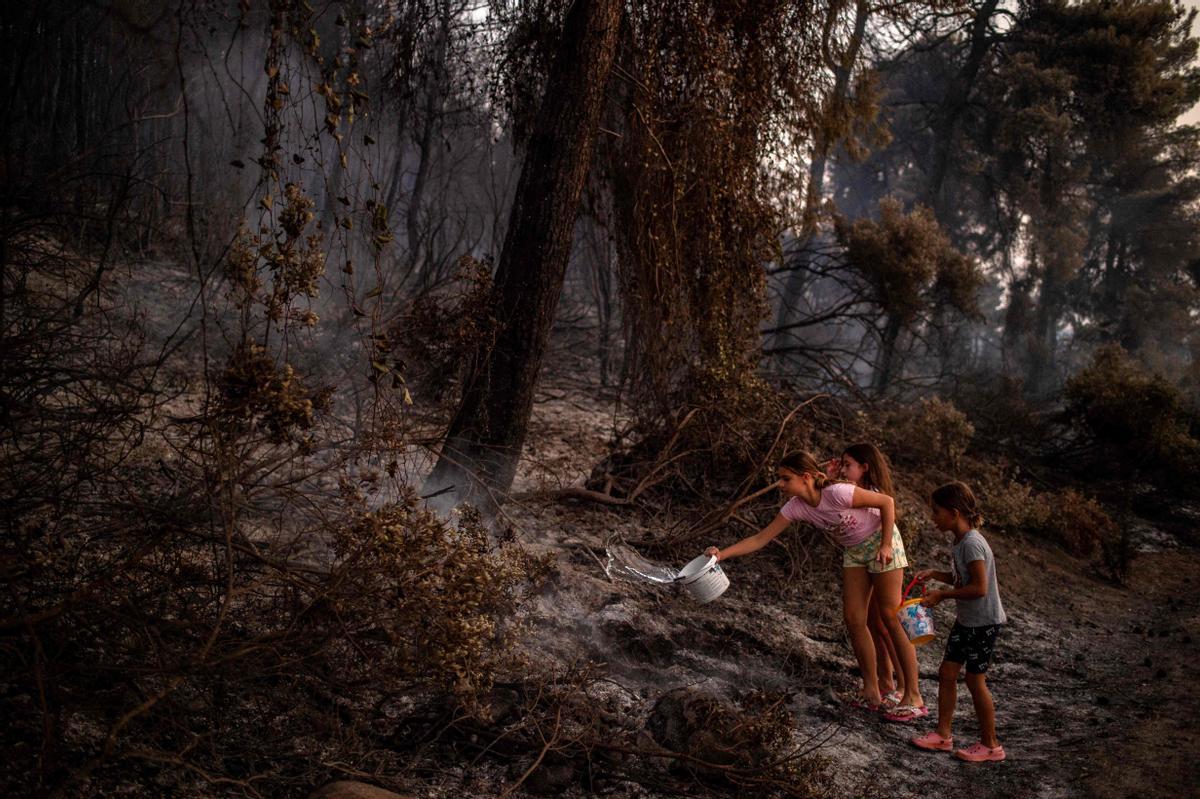 Unos niños refrescan la tierra tras el paso del incendio en Eubea.
