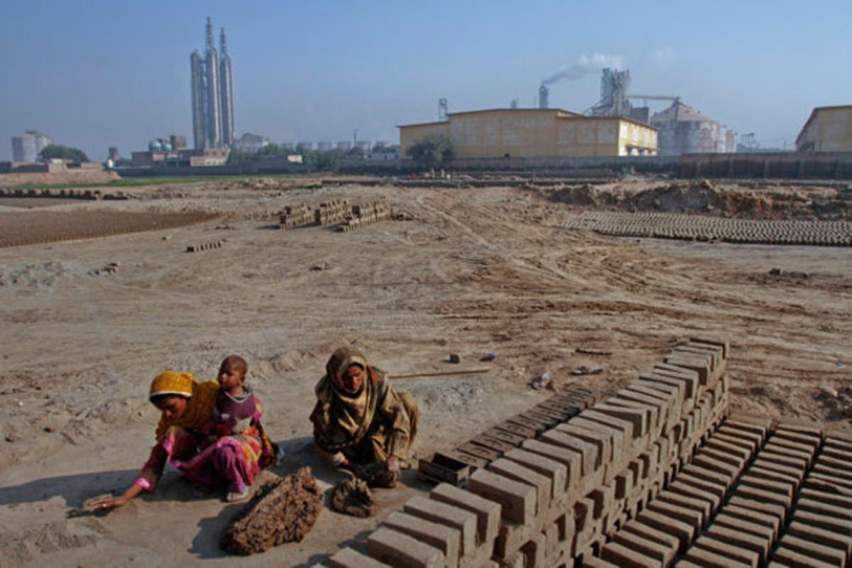 Dues dones fabriquen totxos prop d’una refineria, a Multan (Pakistan).