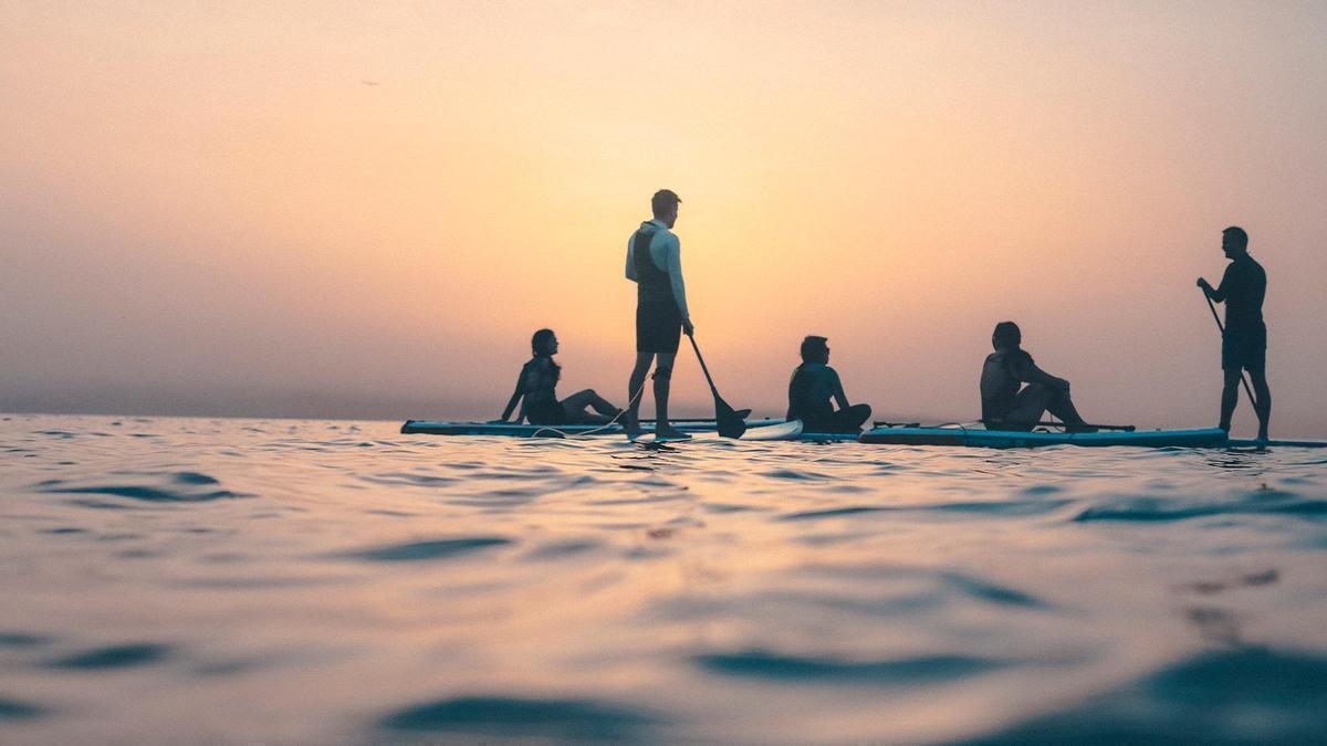 Un grupo de personas practicando paddle surf al atardecer