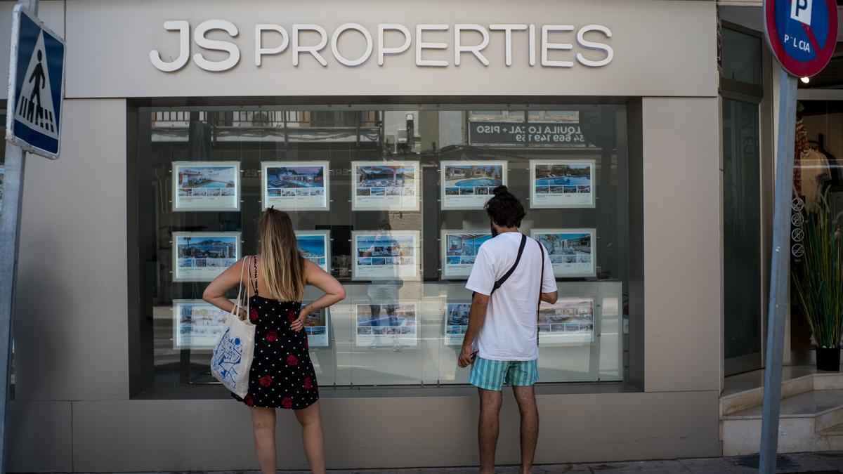 Archivo - Dos personas observan inmuebles en alquiler y en venta en un escaparate de una inmobiliaria ubicada en Palma.