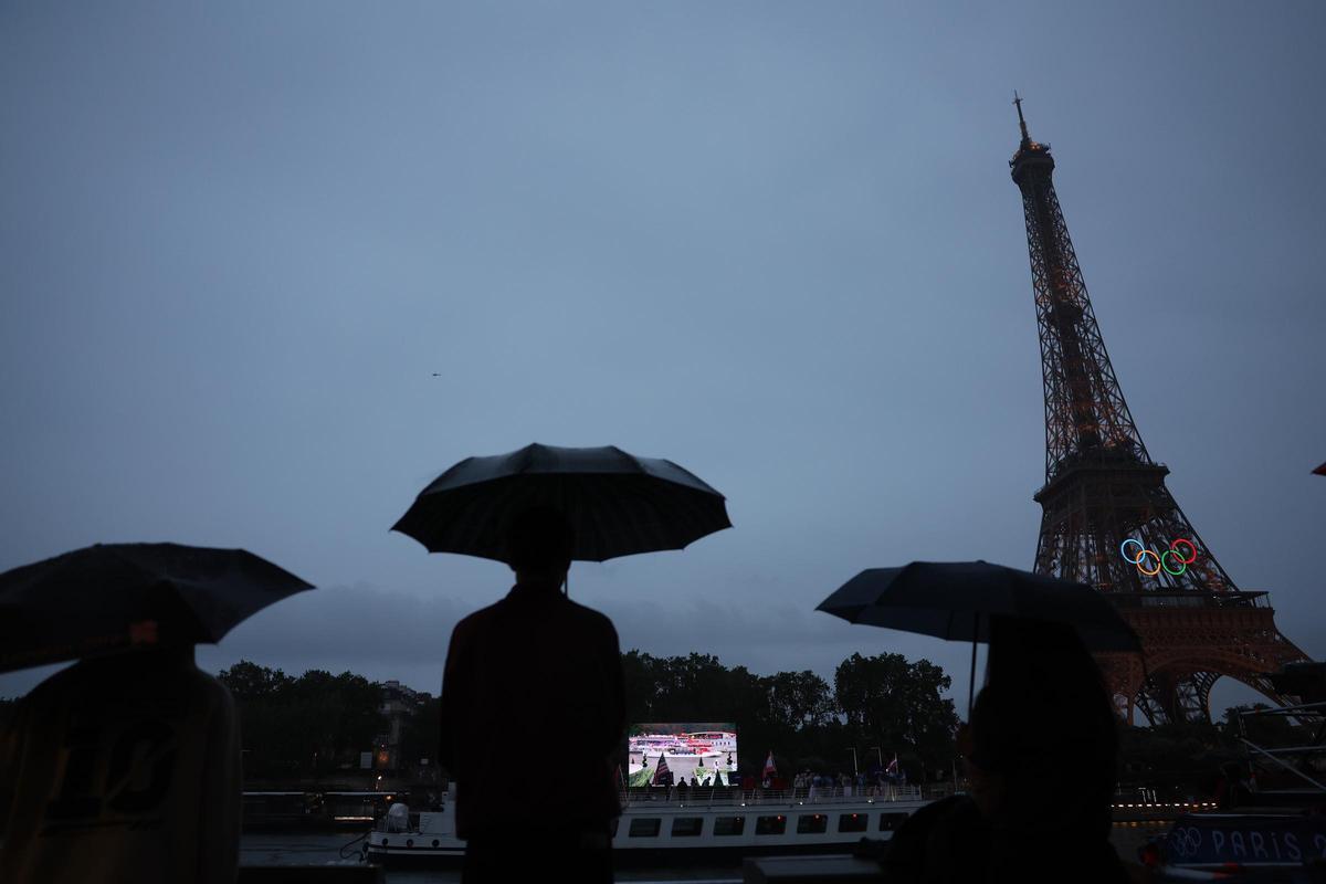 Asistentes protegidos con paraguas junto al río Sena con la Torre Eiffel de fondo durante la ceremonia de inauguración de los Juegos Olímpicos de París 2024