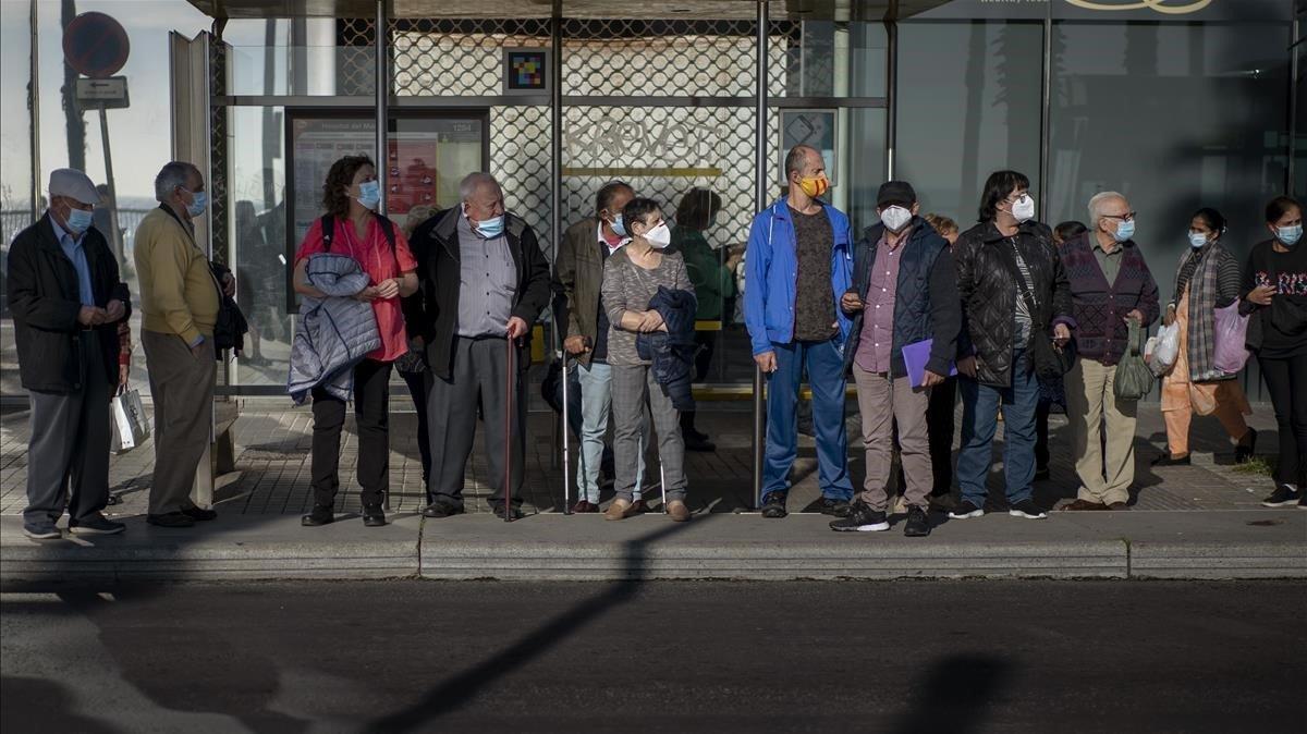 Varios ciudadanos esperan el bus en una parada de Barcelona.