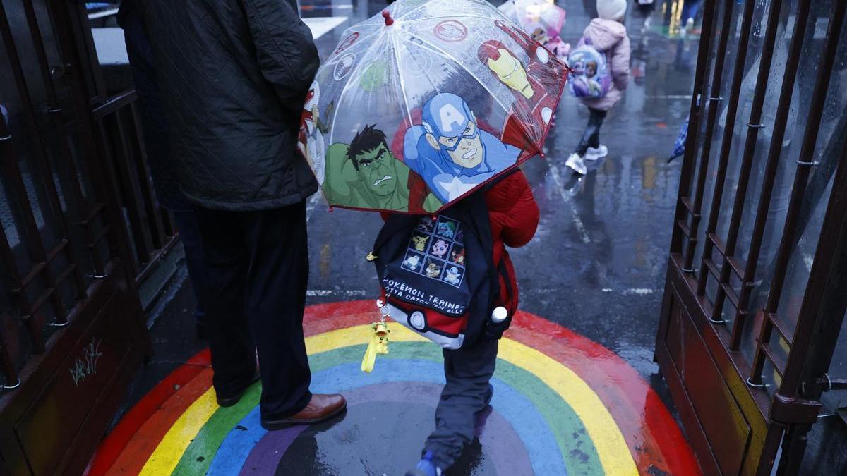 Un niño entrando en un colegio una mañana lluviosa.