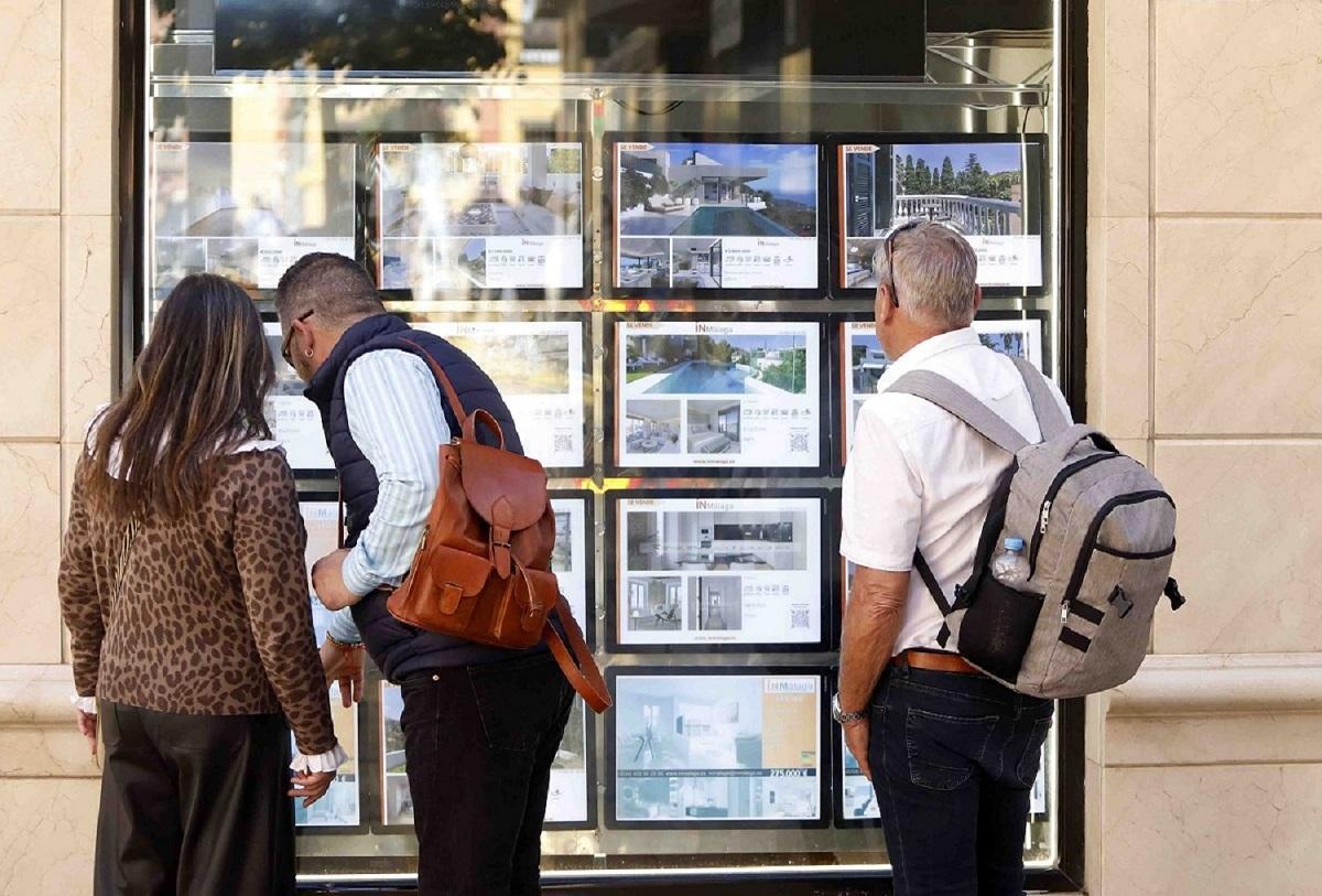 Varias personas observan en un escaparate de una inmobiliaria.
