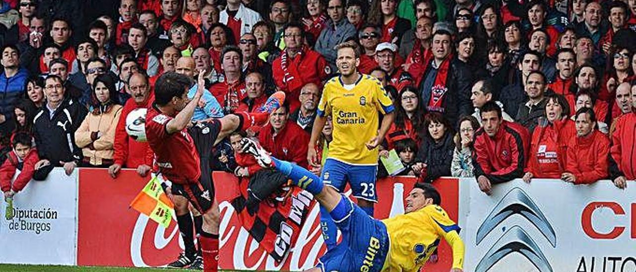 Vicente Gómez pugna por el balón con un jugador del mirandés ante la mirada de Dani Castellano, el 19 de abril de 2014 en Anduva, con el público de pie.