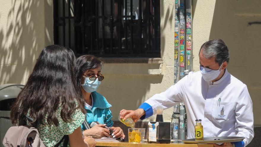 Un camarero sirve un refresco a dos personas en una terraza