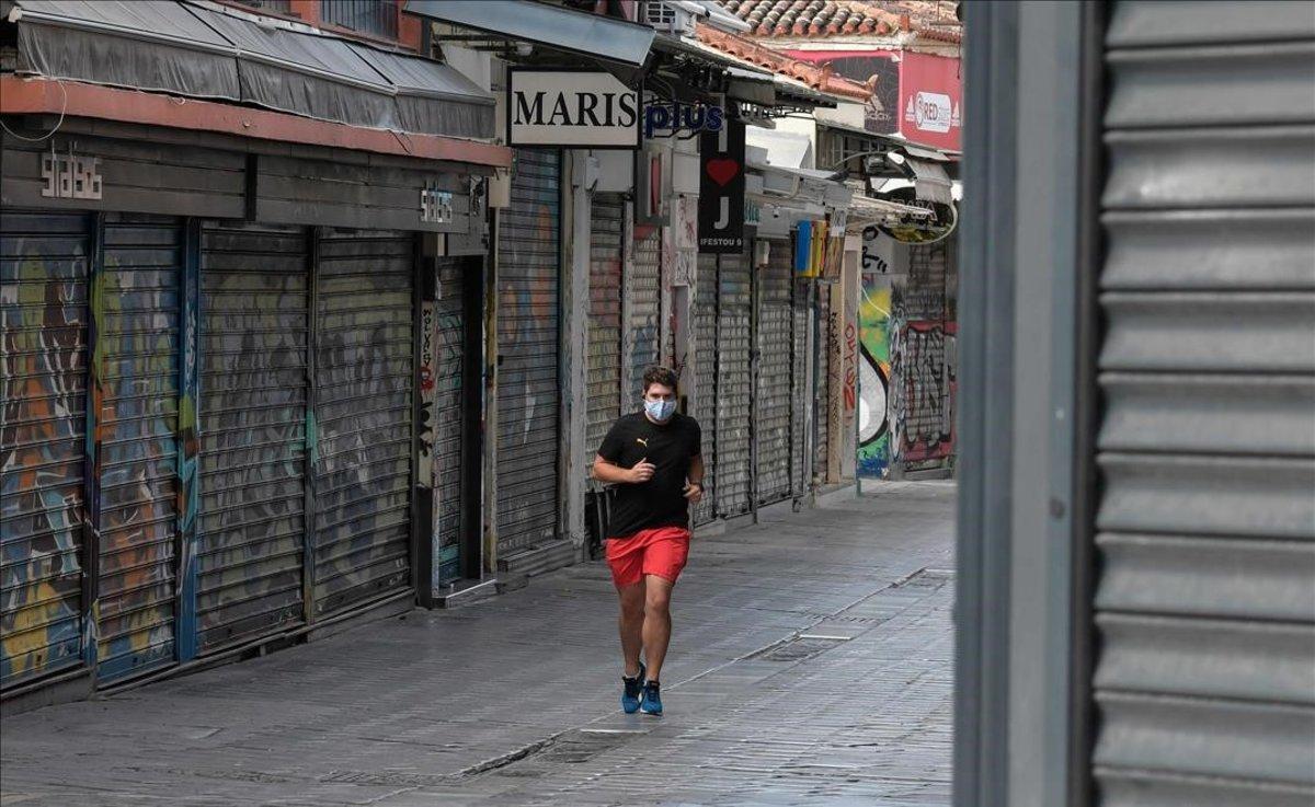 Un hombre practica deporte por una calle comercial con las tiendas cerradas, en el centro de Atenas.
