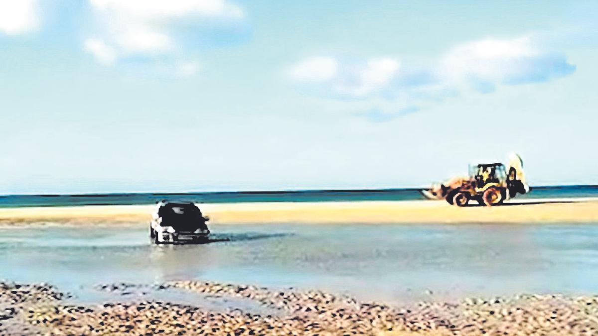 Imagen del vehículo atrapado en la arena de la playa de La Barca mientras el tractor acude a su rescate.