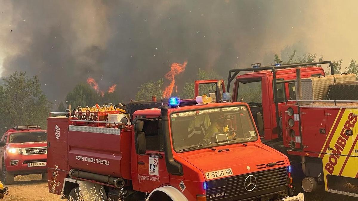 Imagen de las llamas detrás de los vehículos de los bomberos que trabajan en la extinción del incendio forestal de Caudiel