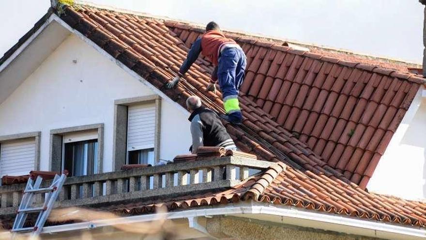 Unos vecinos recomponen el tejado de su casa, en Meis. // Iñaki Abella