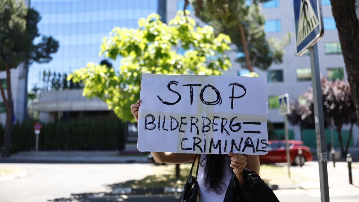 Una mujer sostiene una pancarta a las puertas del hotel de Madrid donde desde hoy jueves, cientos de representantes del más alto nivel del mundo empresarial, financiero, político y académico de Europa y EEUU se dan cita en la septuagésima Reunión Bilderberg.