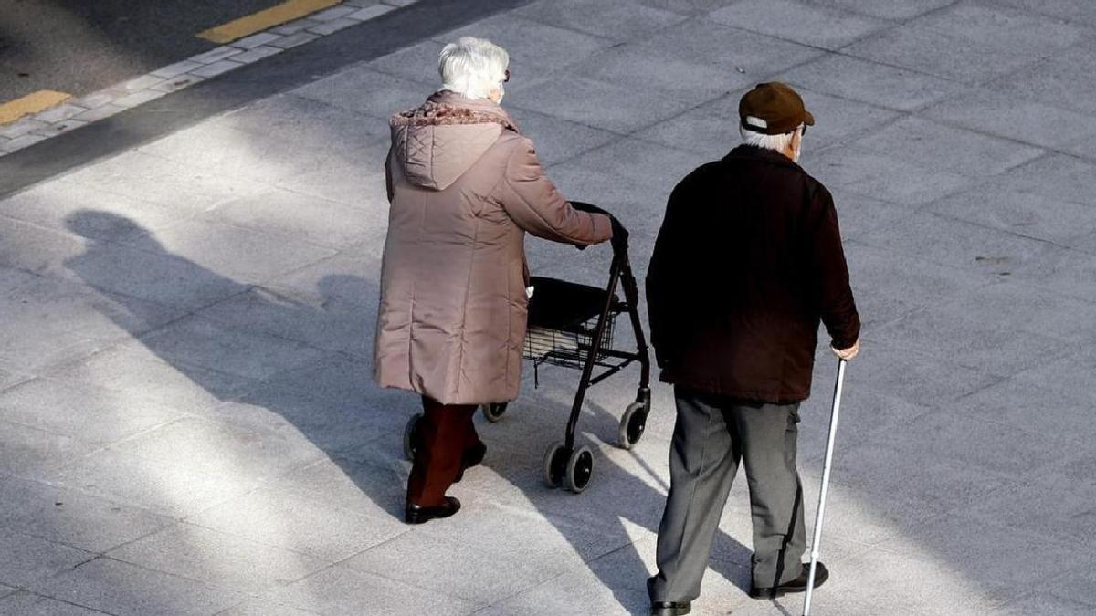 Una pareja de jubilados pasea por una calle.
