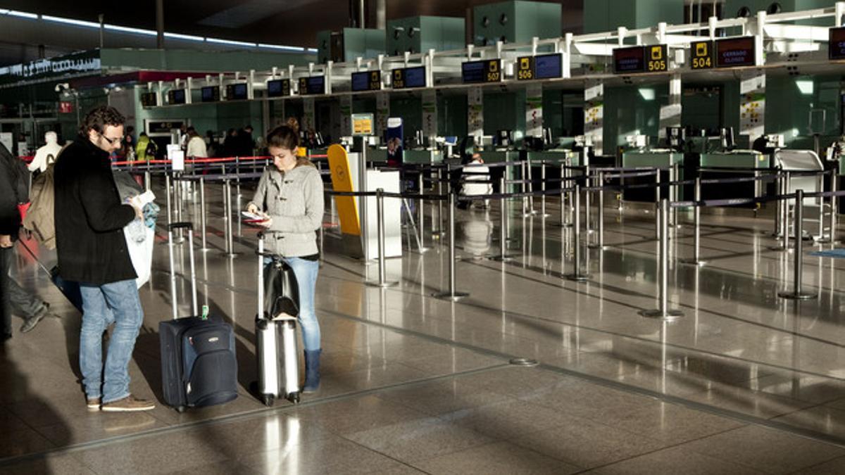 Dos jóvenes esperan para facturar en el aeropuerto de El Prat.