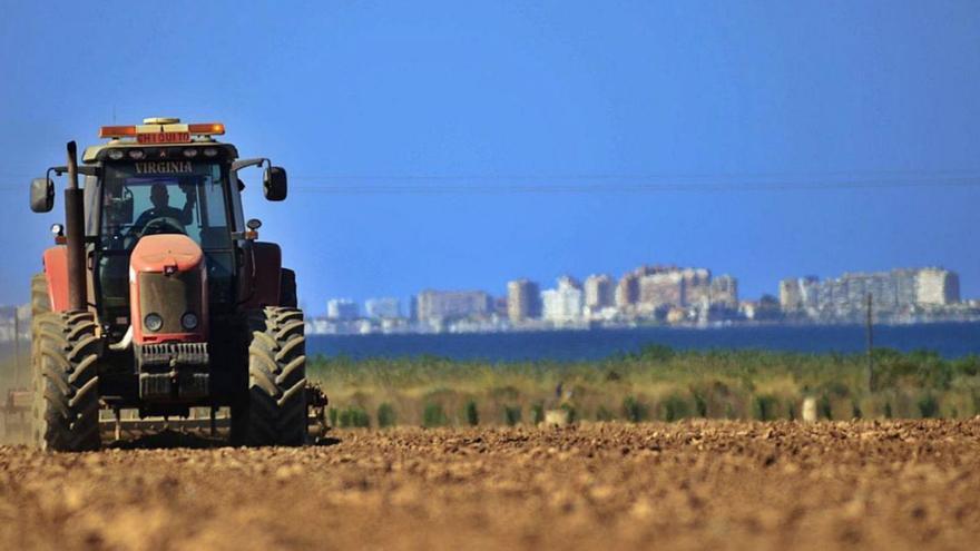 Un agricultor conduce un tractor en terrenos de cultivo frente al Mar Menor. | IVÁN URQUÍZAR