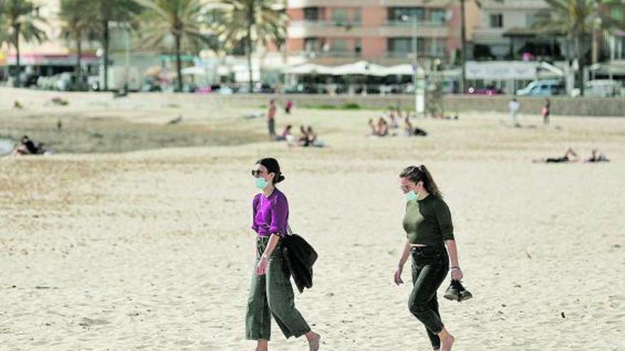 Dos jóvenes caminan por una playa con las preceptivas mascarillas.