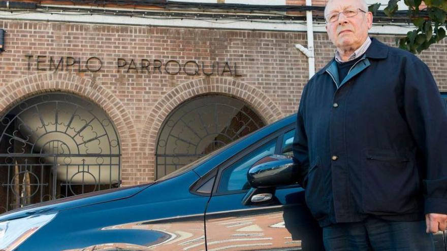 El párroco José Manuel Pidal posa junto a su coche delante de la iglesia nueva de Colloto.