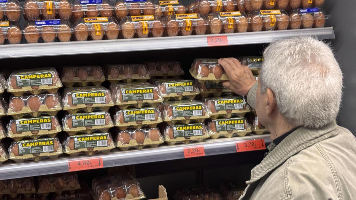 Un hombre cogiendo una docena de huevos de la estanteria de un supermercado