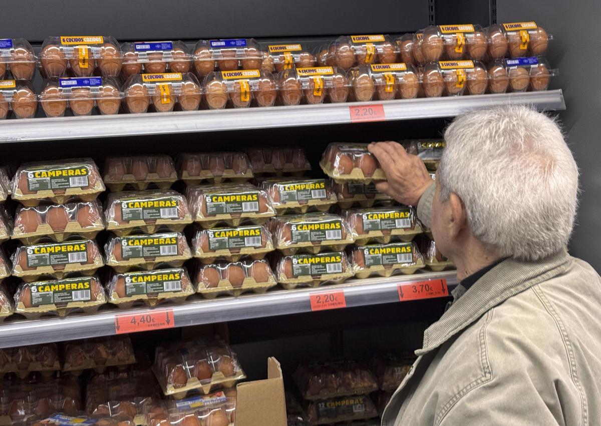 Un hombre cogiendo una docena de huevos de la estanteria de un supermercado, en una imagen de archivo.