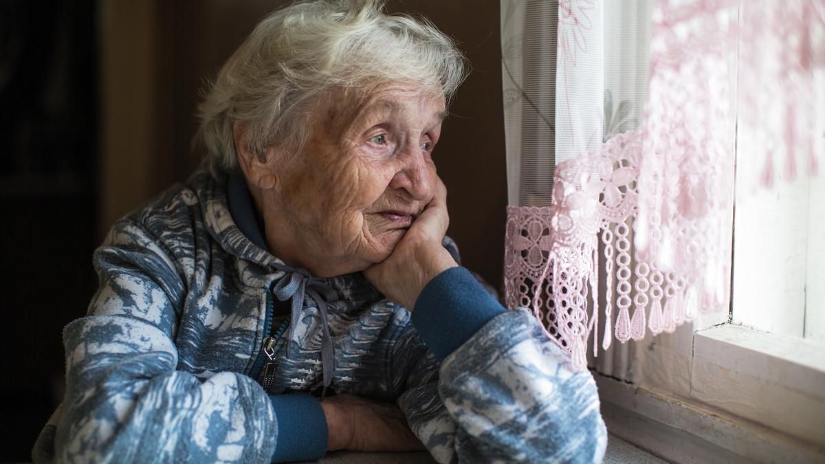 Una mujer mayor mita por la ventana de su casa