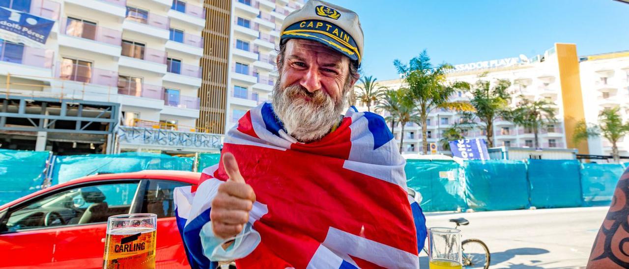 Un turista británico envuelto con la bandera de su país se toma una cerveza en una terraza de Benidorm. | DAVID REVENGA