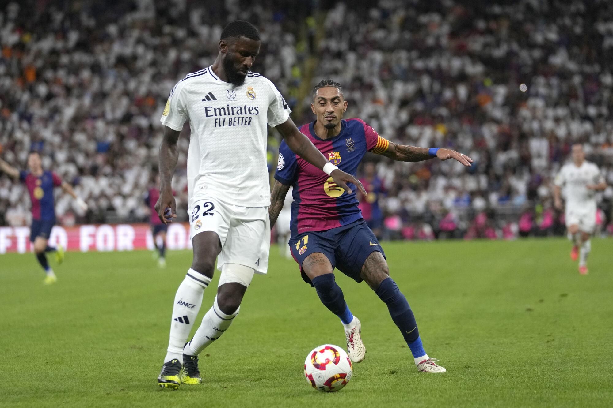 Real Madrid's Antonio Rudiger, left, challenges for the ball with Barcelona's Raphinha during the Spain Super Cup final soccer match between Real Madrid and Barcelona at King Abdullah Stadium in Jeddah, Saudi Arabia, Sunday, Jan. 12, 2025. (AP Photo/Altaf Qadri)