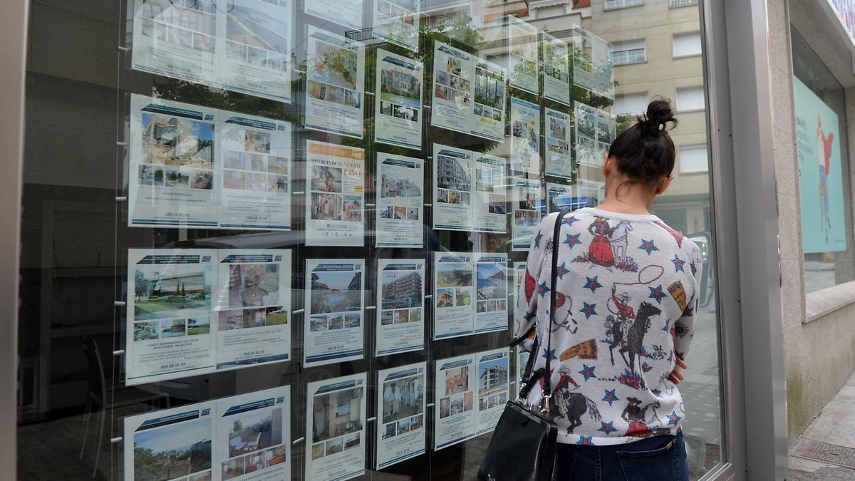 Una mujer mira los anuncios de viviendas en el escaparte de una inmobiliaria.