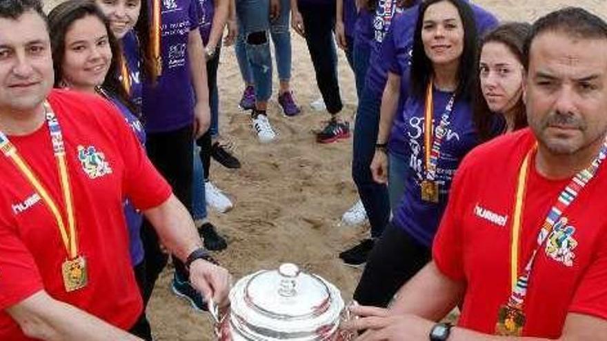 Los técnicos y jugadoras del Mavi junto a la Copa de la Reina en el arenal de San Lorenzo, en Gijón.