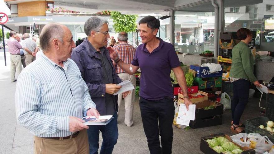 El número tres de Unidos Podemos y coordinador de IU, Manuel González Orviz, en el centro, y el diputado de Podemos Enrique López -derecha-, reparten propaganda electoral en el mercado de Pola de Siero.