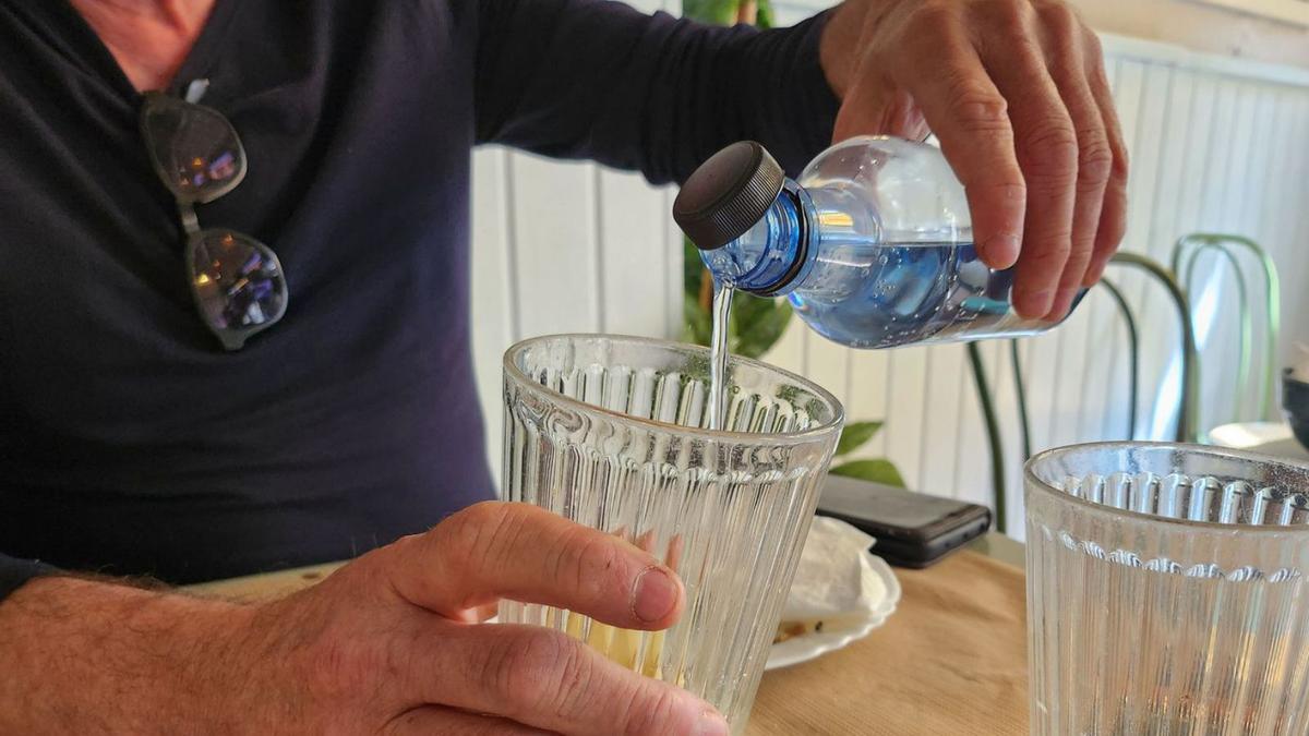 Un hombre se sirve agua en un vaso en la mesa de una cafetería de Vigo.