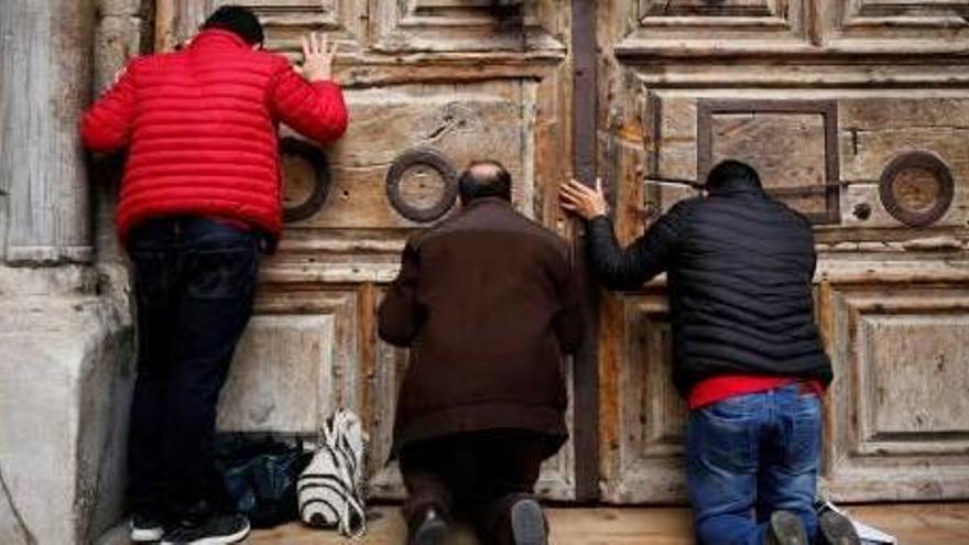 Tres persones preguen davant la porta tancada del Sant Sepulcre