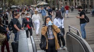 Una mujer se coloca la mascarilla antes de entrar en el metro, en La Rambla de Barcelona.