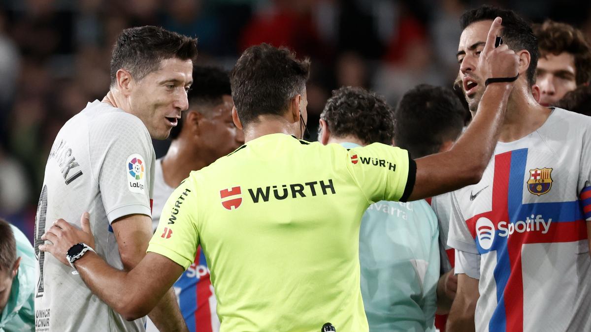 El delantero del FC Barcelona Robert Lewandowski (i) conversa con el árbitro Gil Manzano (c) al ser expulsado, durante el partido de Liga en Primera División que Osasuna y FC Barcelona disputan este martes en el estadio de El Sadar, en Pamplona.