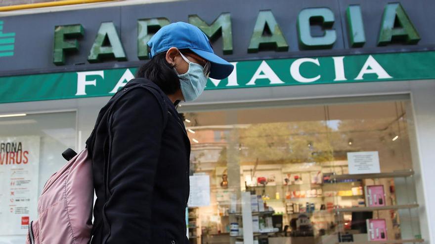 Una viandante, protegida con guantes y mascarilla, pasa por delante de una farmacia del centro de Madrid.