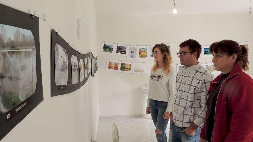 El alcalde de Vecilla de la Polvorosa, Rubén Bécares, observa la exposición de fotografías junto a varias vecinas y, a la derecha, señala una de las imágenes.