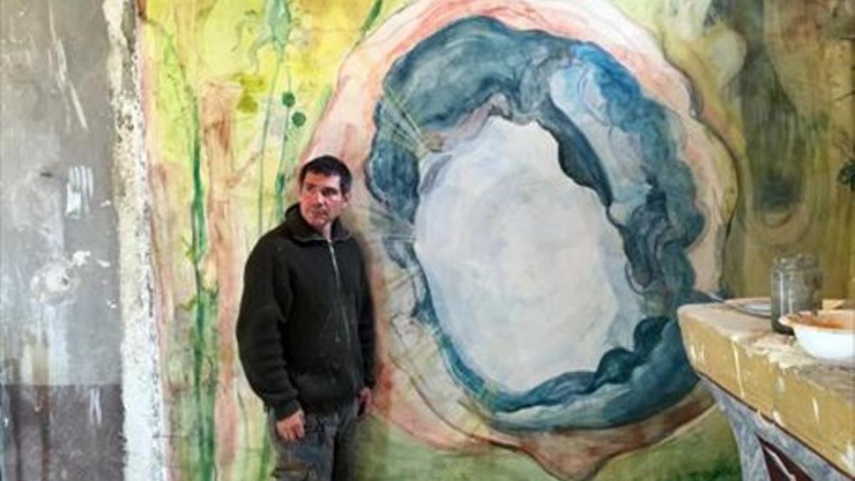 El artista Santi Moix, junto a uno de los frescos y coloristas murales que ha pintado en la iglesia Sant Víctor de Saurí del siglo XII.