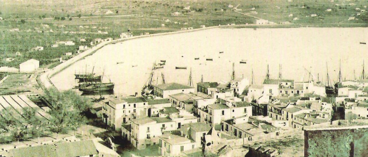 Part de ponent del port d’Eivissa en una imatge de les darreries del segle XIX; es veu el Teatre Pereira encara en construcció. La drassana encara era al Racó des Moll. Vora la carretera de Santa Eulària, únicament hi ha l’Escorxador.