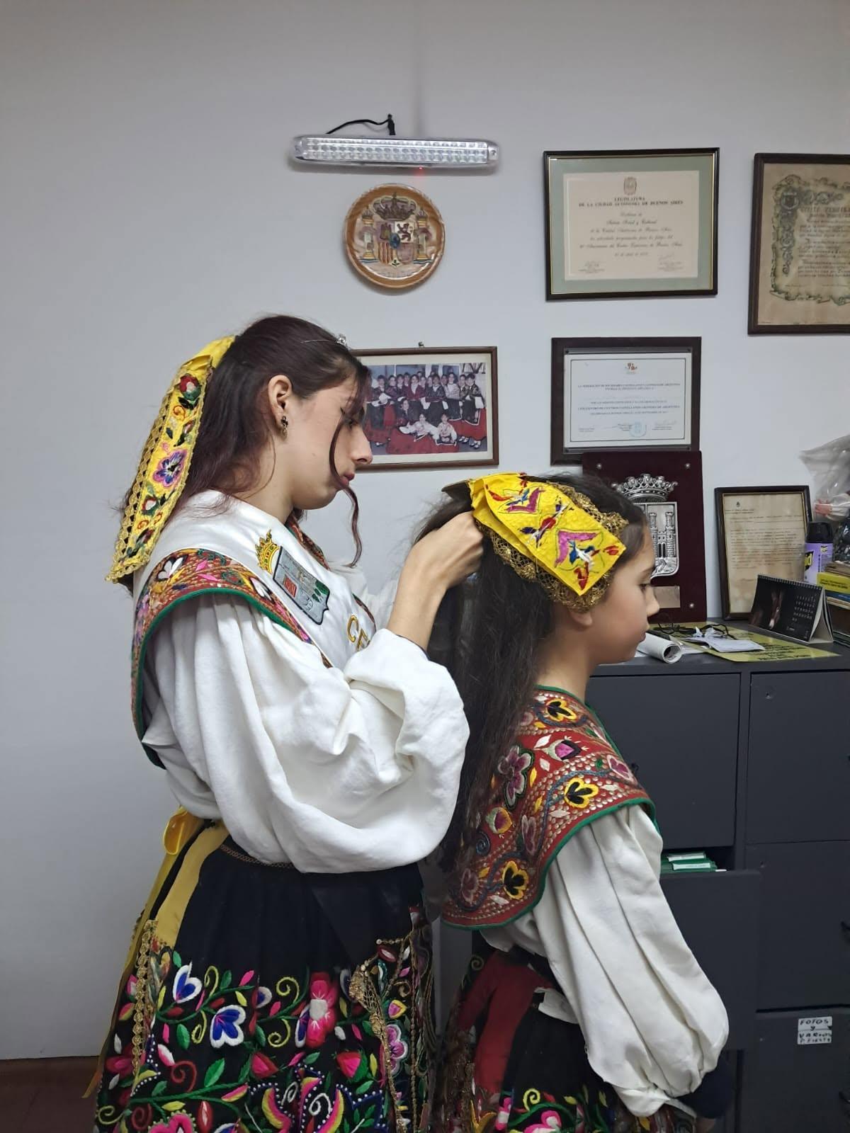 Una socia coloca el tocado del traje regional a una niña.