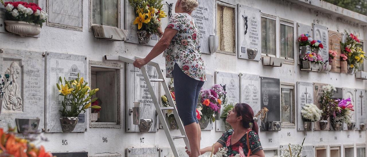 Dos mujeres ponen flores en un nicho del cementerio de Santa Lastenia.